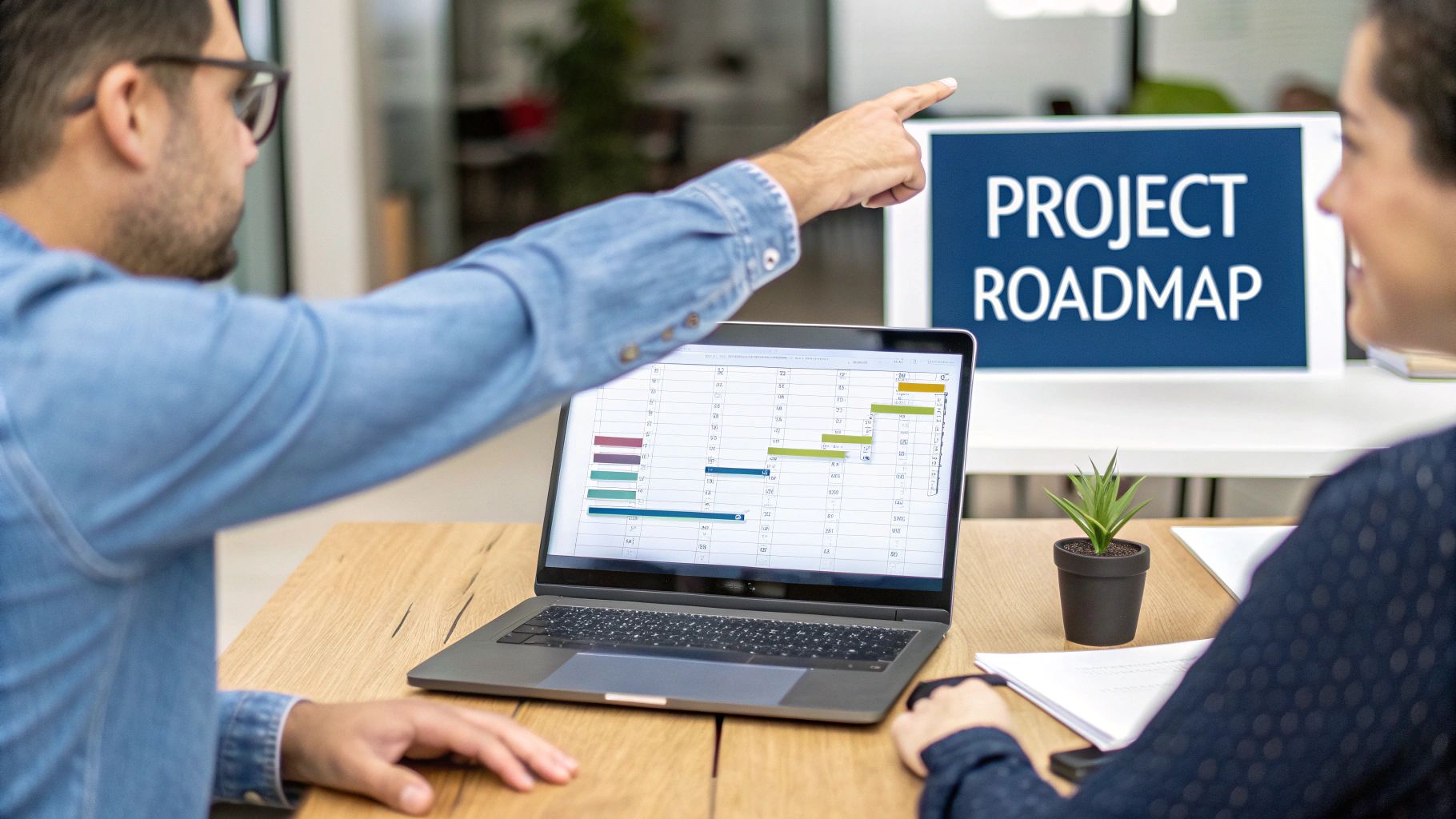 Two colleagues discussing a project roadmap shown on a large screen and a laptop.