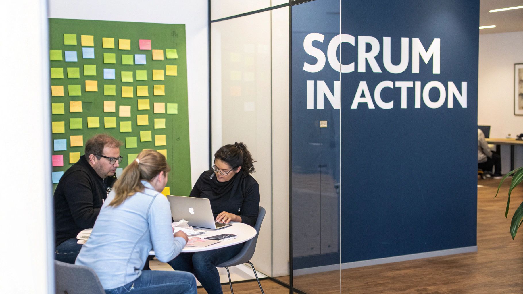 Three people work together in an office, one on a laptop, with a sticky note board and 'SCRUM IN ACTION' sign.