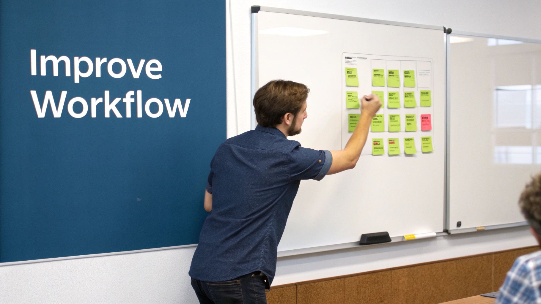 A man in a denim shirt improves workflow, pointing at green sticky notes on a whiteboard.